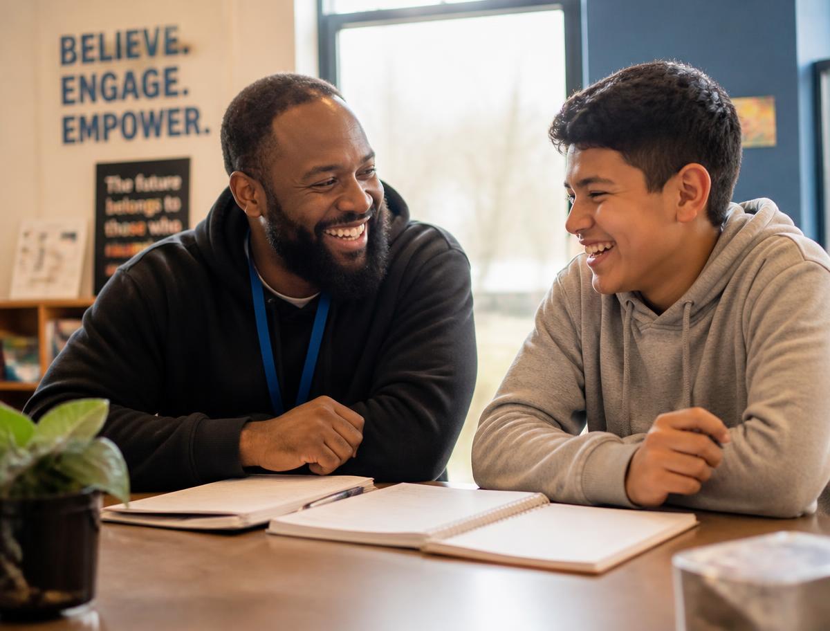 A mentor and a teenage student laughing together over notebooks